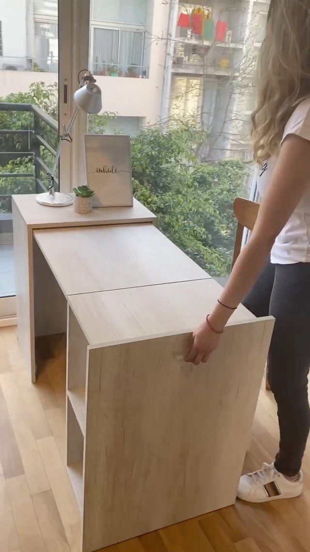 Woman unfolding a light wood compact desk in a bright room with wooden floors.