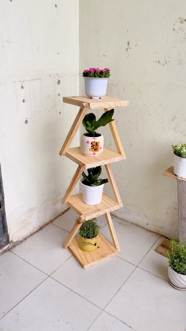 Wooden tiered plant stand with potted greenery placed in a white room corner.