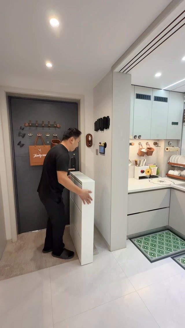Man standing by a white pull-out shoe rack and wall hooks in entryway