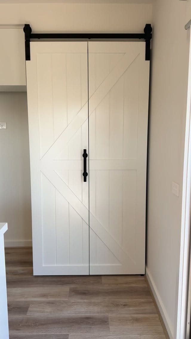 White sliding barn doors with black hardware on a light wood floor.