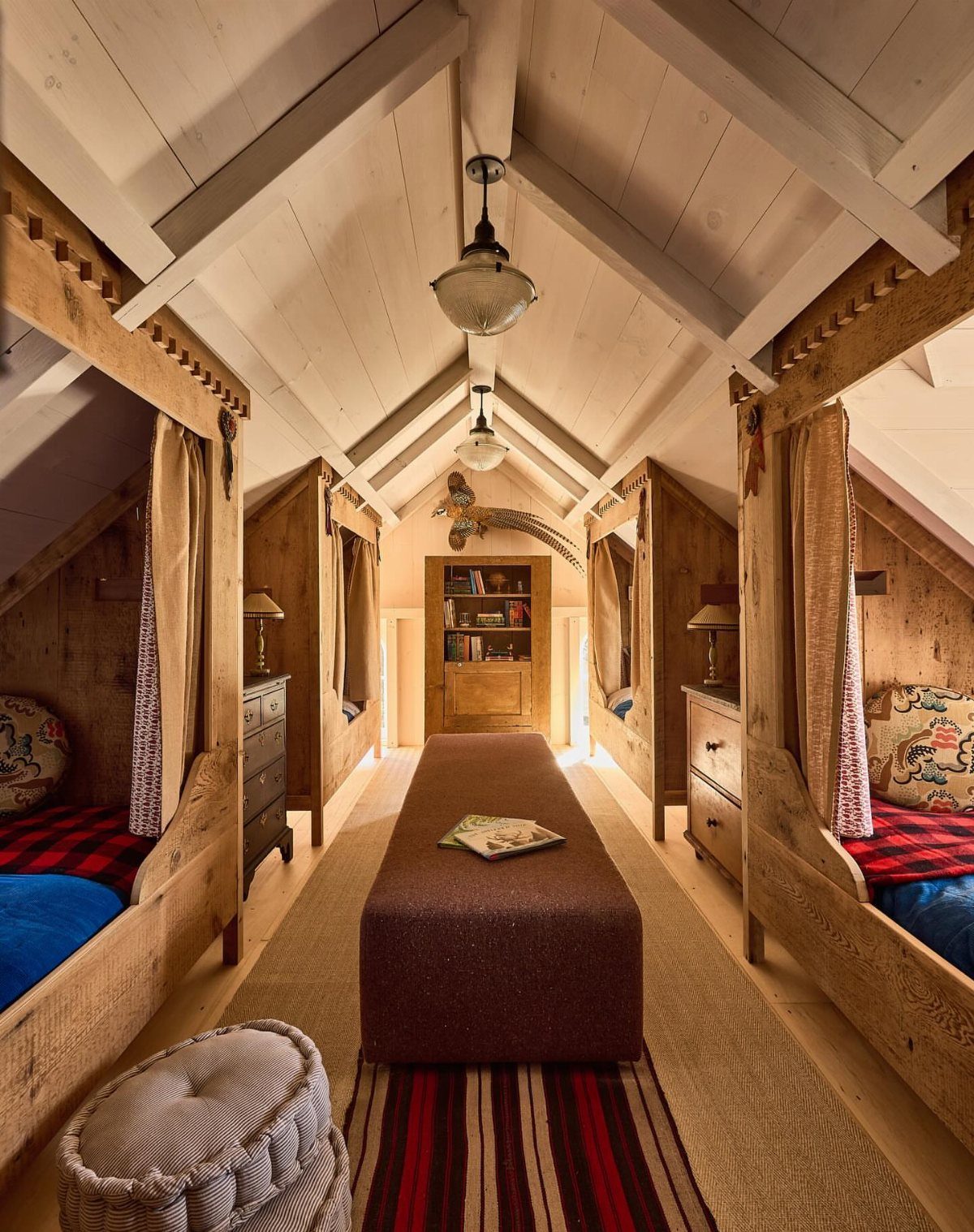 Wooden sleeping pods and a central daybed in a vaulted barn loft room.