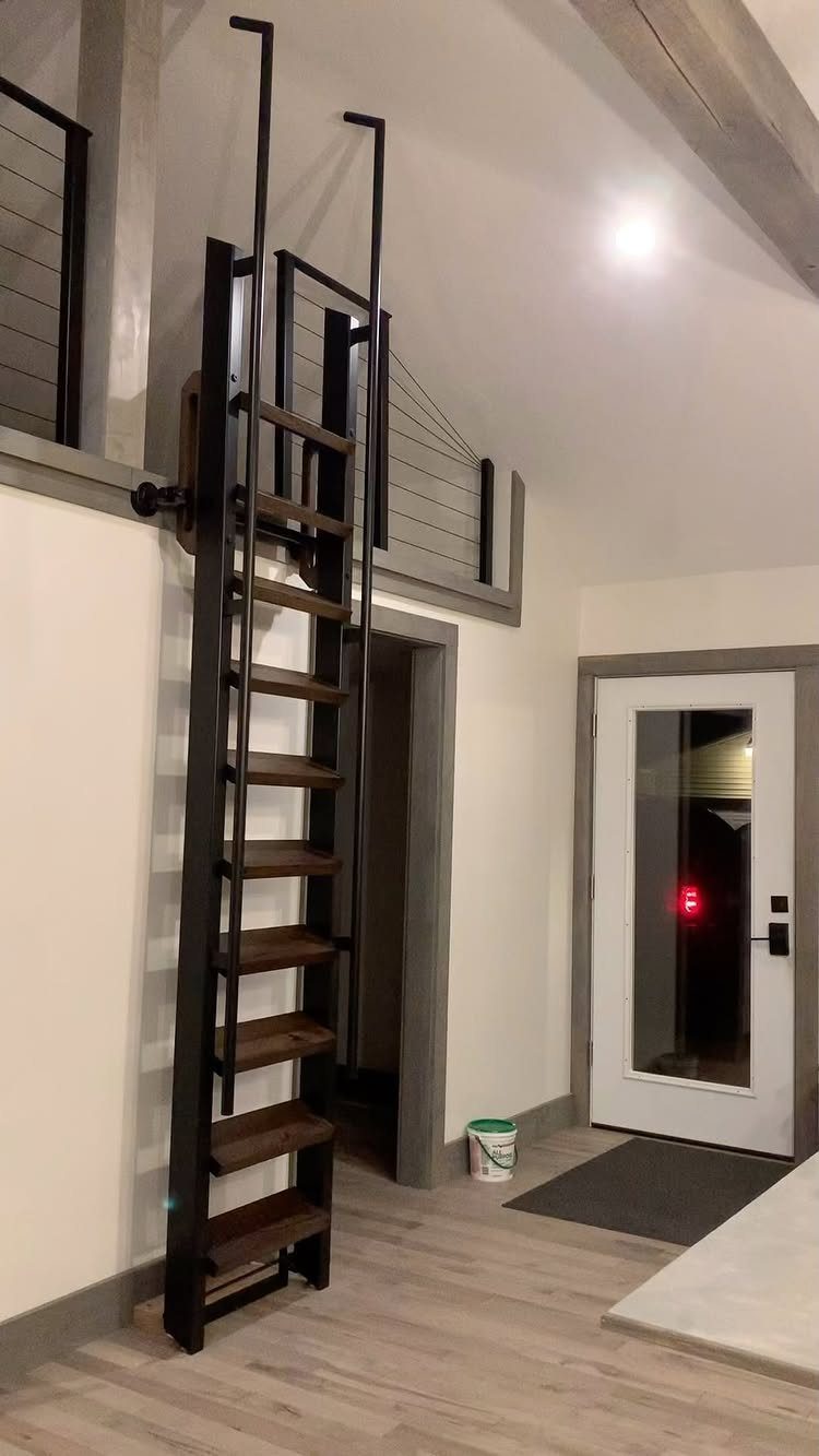 Black metal ladder with wooden steps leading to a modern barn loft apartment.