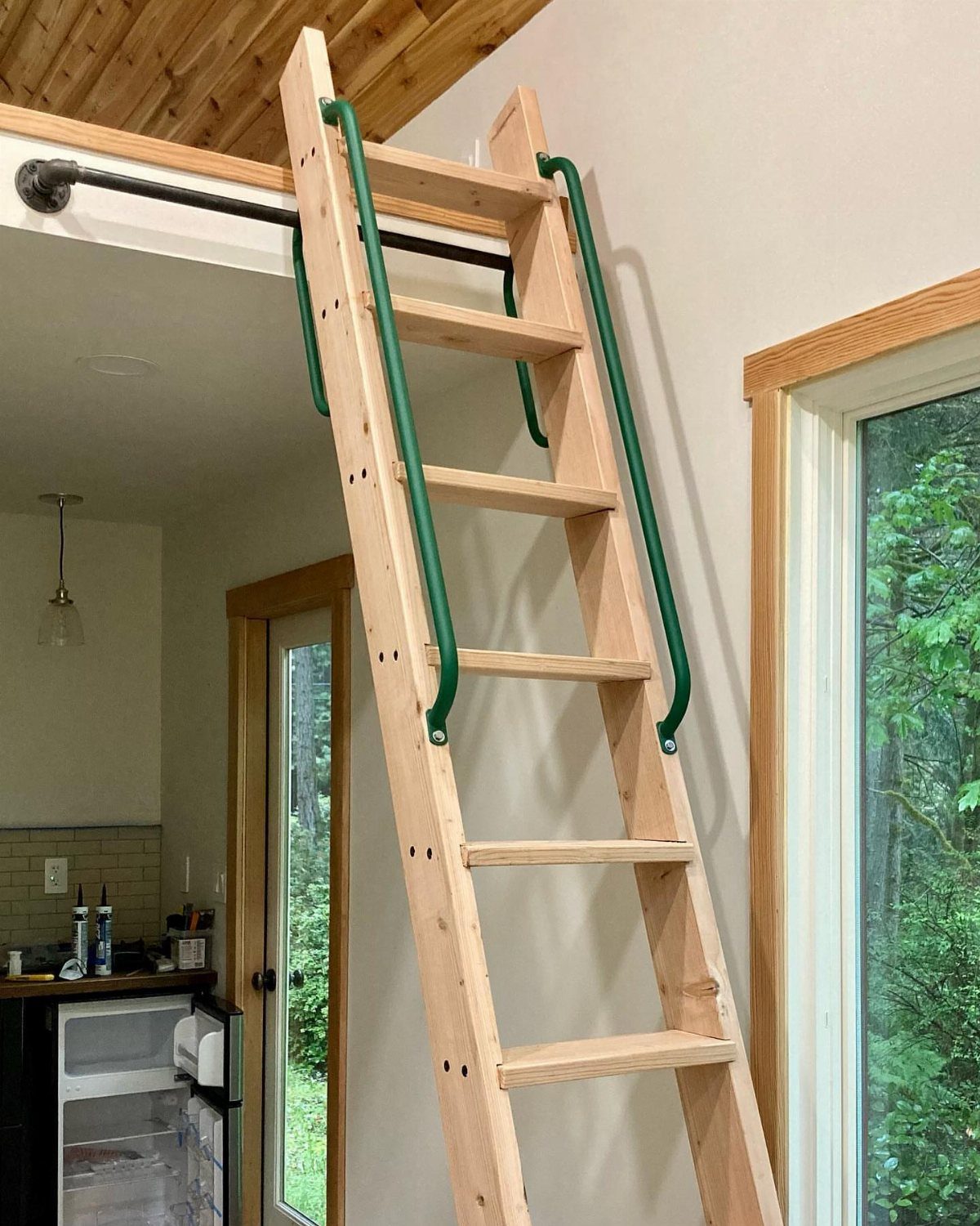Wooden loft ladder with green metal handrails leading to an upper level.