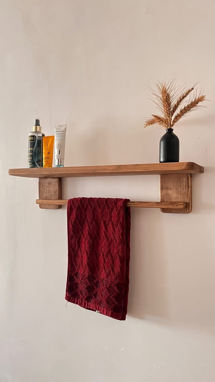 Wooden wall shelf with a towel bar holding a red textured towel and toiletries.