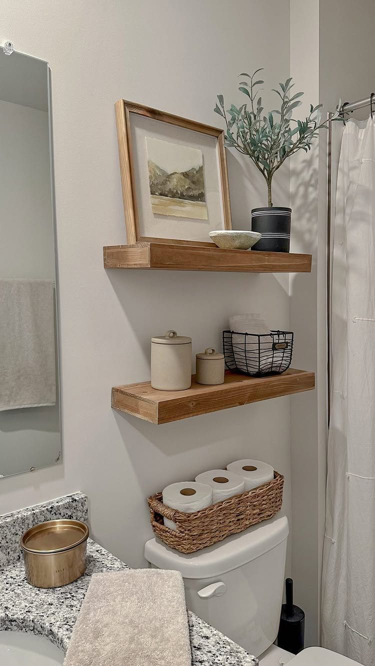 Wooden floating shelves above a toilet holding decor, jars, and a small plant.