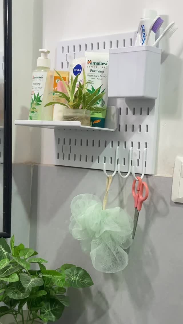 White plastic pegboard on a wall holding skincare, a plant, and bath accessories.
