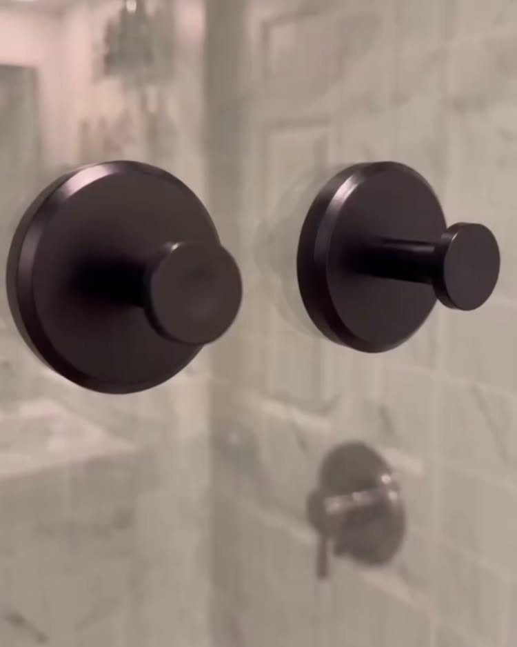 Two matte black circular wall hooks mounted on a white marble tiled wall.