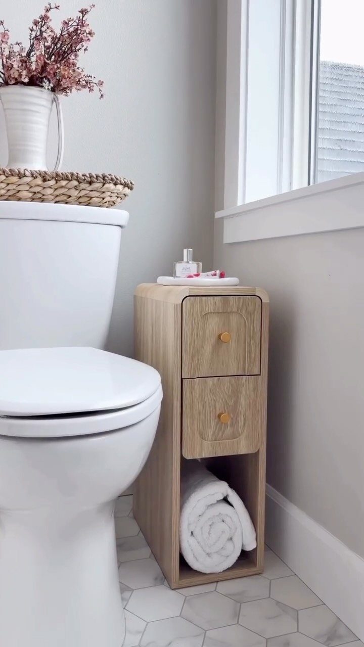 Small light-wood storage cabinet with drawers and towel shelf next to a white toilet.