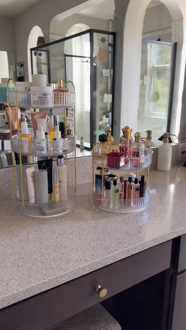 Acrylic rotating organizers holding skincare and perfumes on a white bathroom countertop.