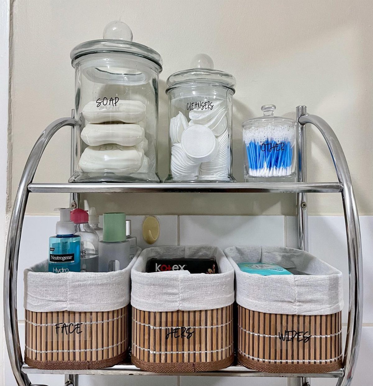 Chrome bathroom shelf with glass jars and labeled bamboo bins for organization.