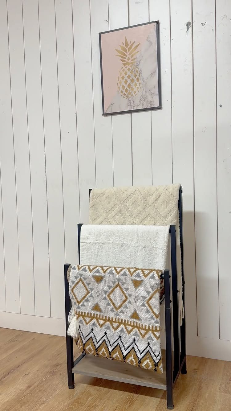 Black metal towel ladder rack with folded towels against a white paneled wall.