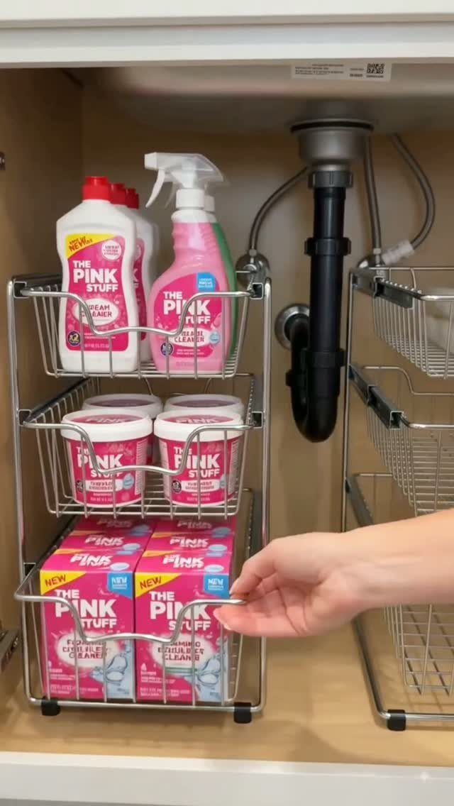 Metal wire organizer holding pink cleaning supplies inside a white bathroom under-sink cabinet.