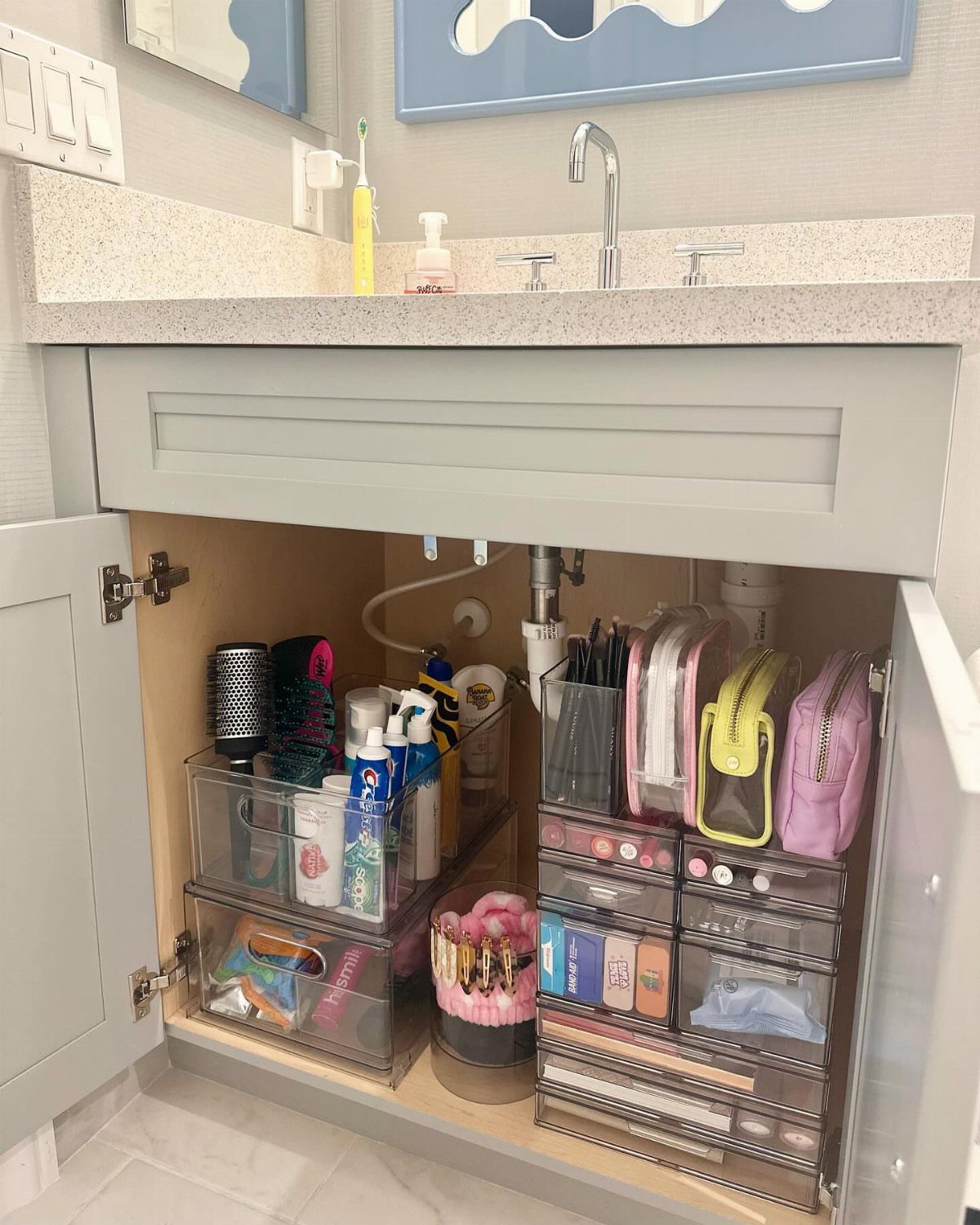 Open bathroom vanity cabinet organized with clear plastic bins and storage drawers.