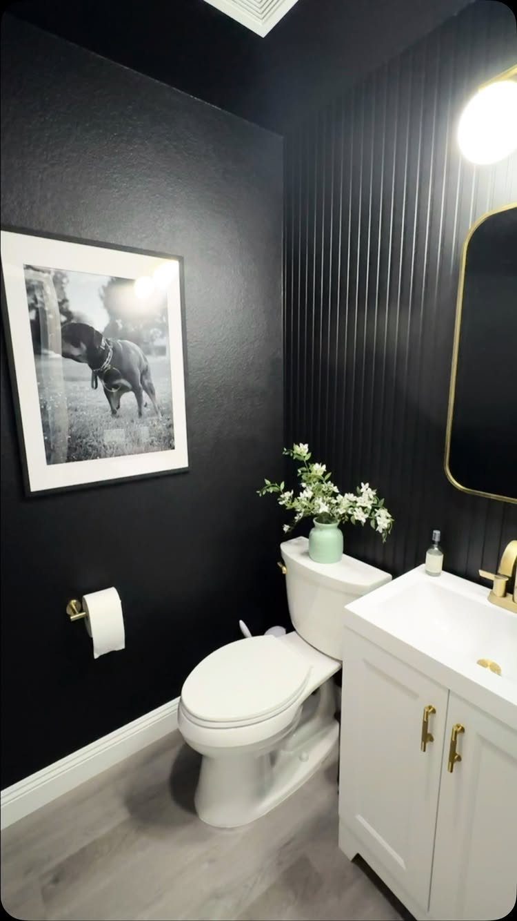 Small bathroom with dramatic black walls, white vanity, and gold accents.