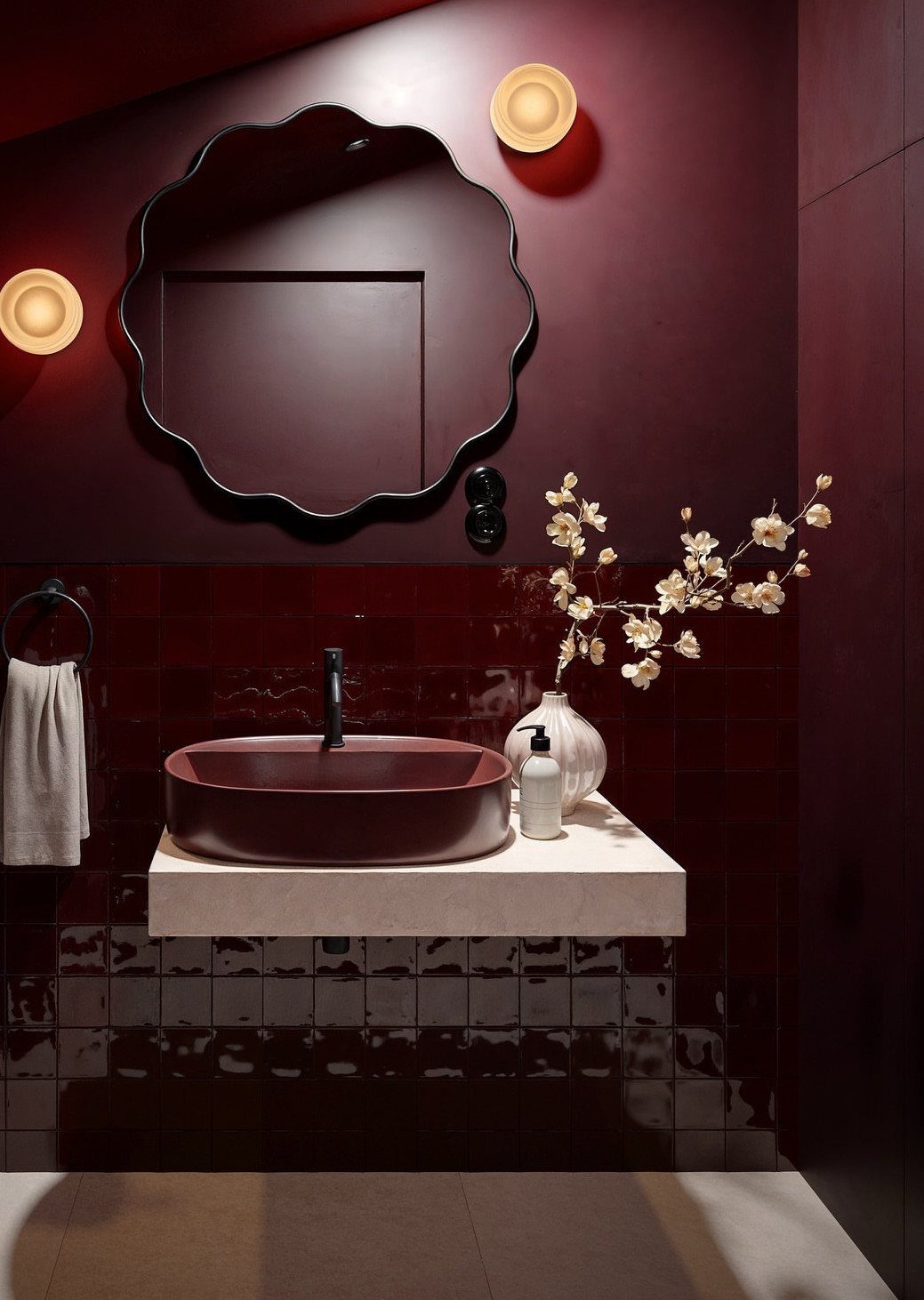 Burgundy bathroom walls and sink with a scalloped mirror and white floral arrangement