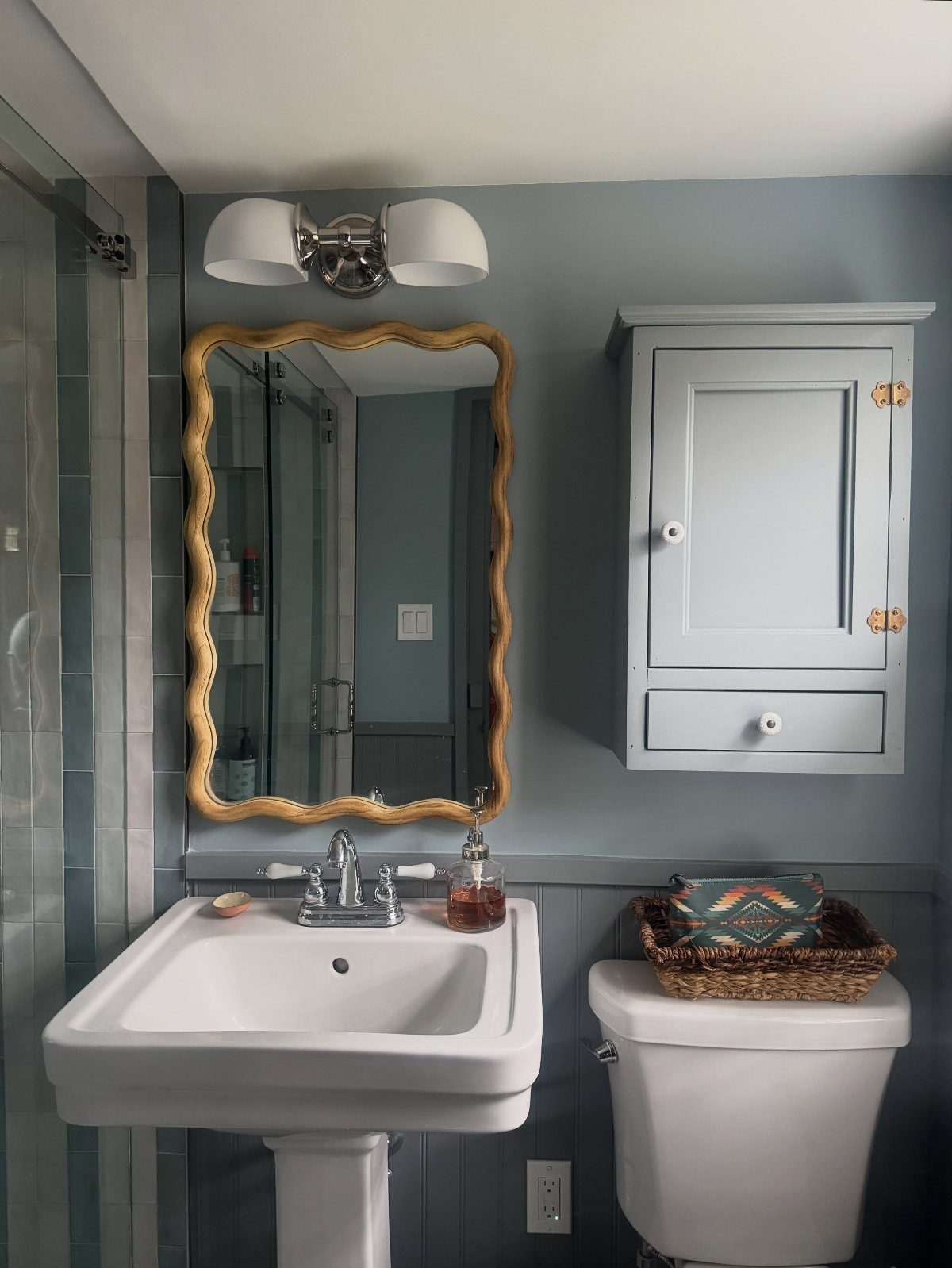 Mid-tone blue bathroom walls with a white pedestal sink and gold-framed mirror.
