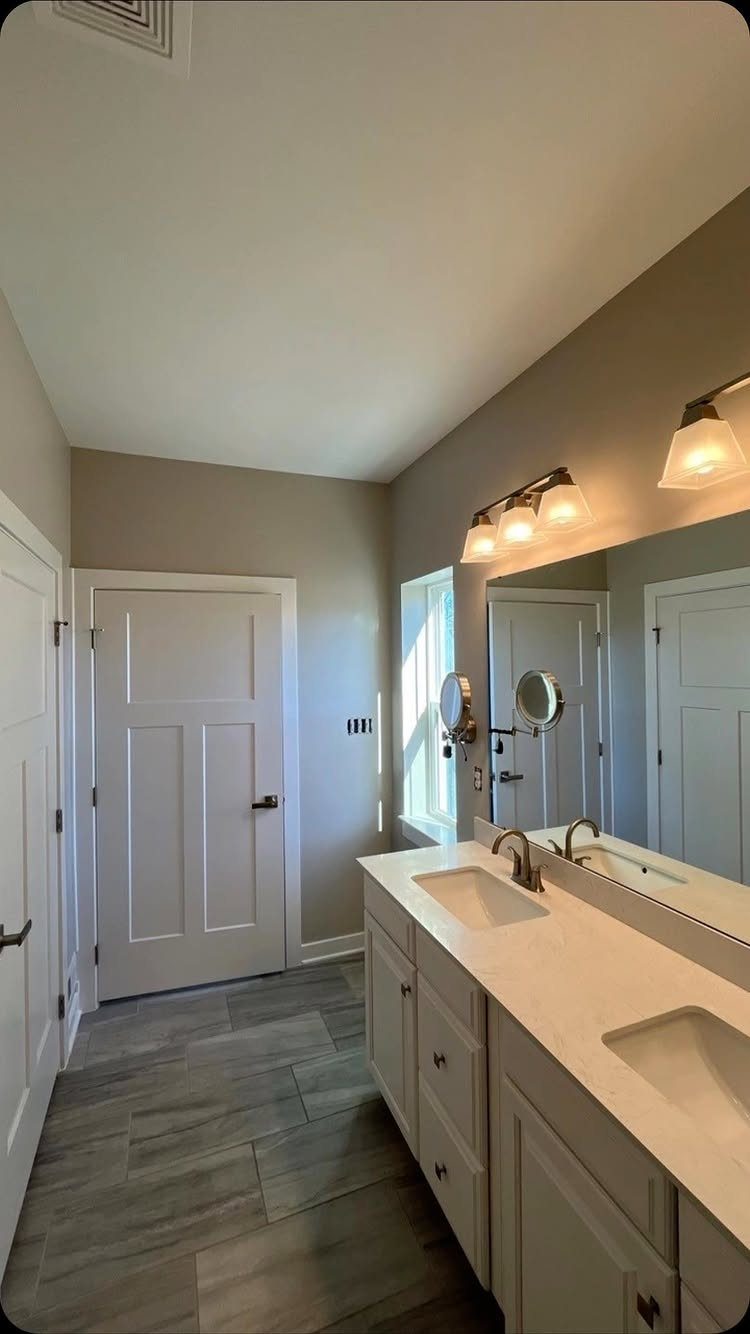 Light greige bathroom walls with white double vanity and grey wood-look tile flooring.
