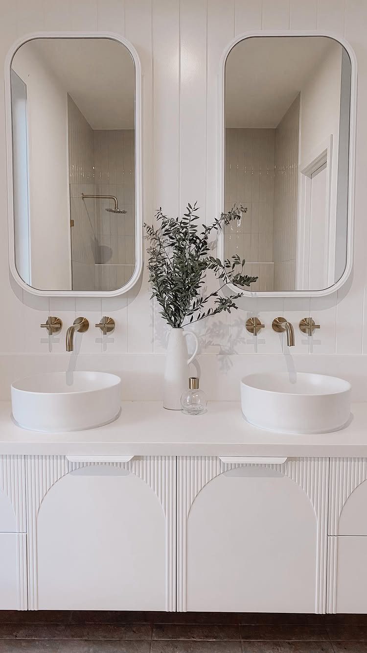 White bathroom vanity with vessel sinks, gold fixtures, and white paneled walls.