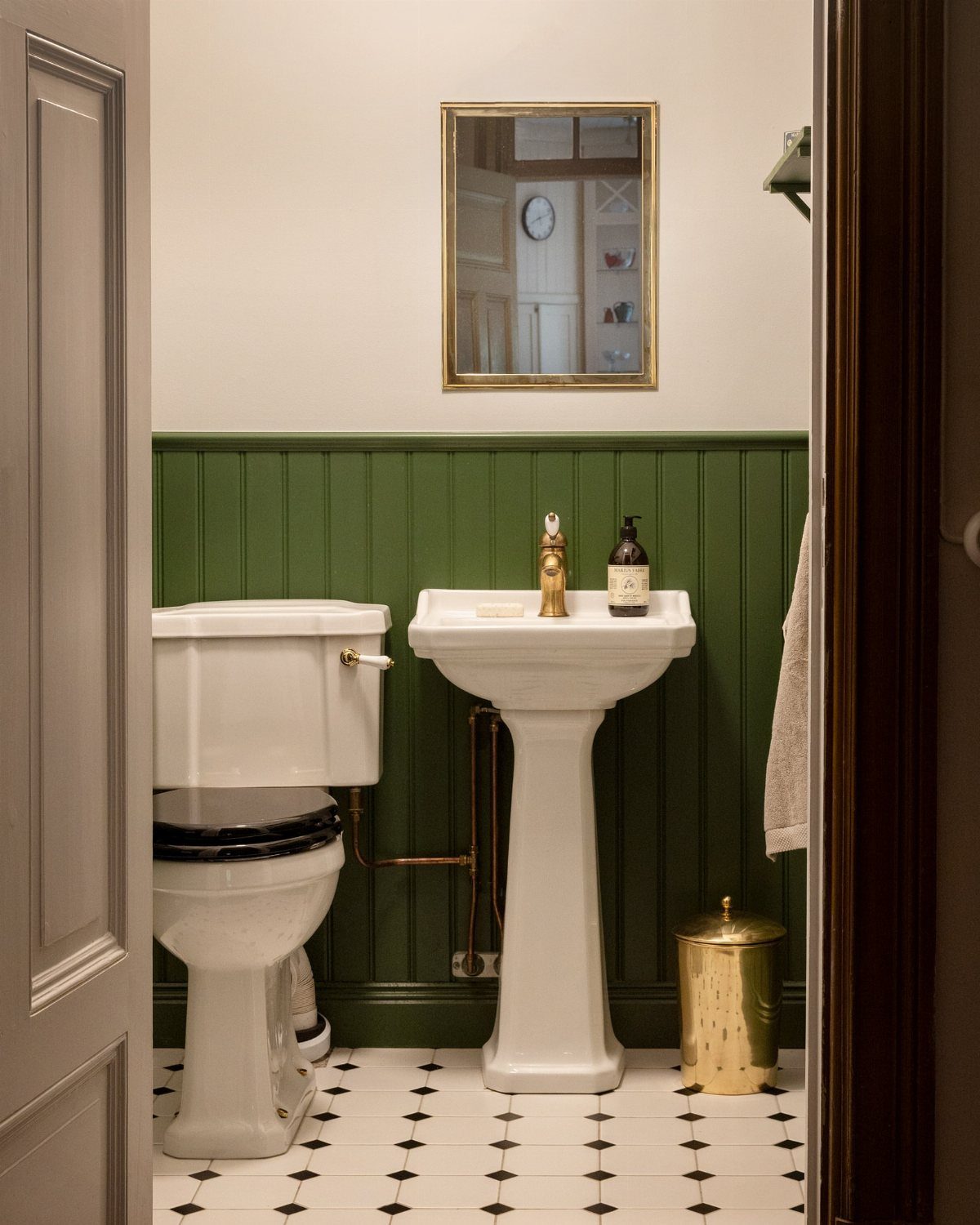 Green beadboard wainscoting in a small bathroom with a white pedestal sink and toilet.
