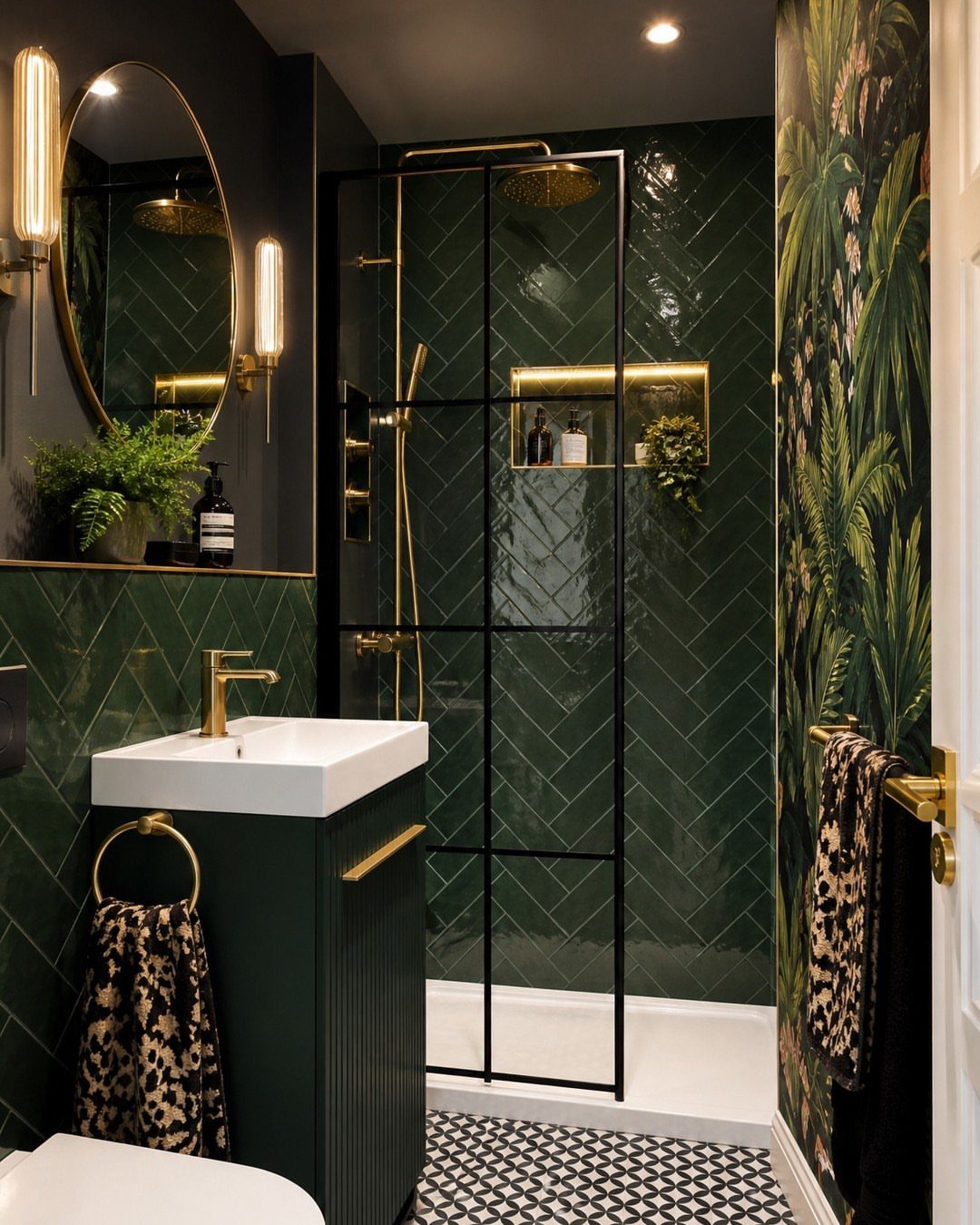 Dark green herringbone tiled wall in a small bathroom with gold fixtures.