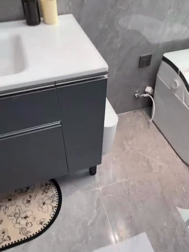 Grey vanity and white washing machine in a small marble-tiled bathroom.
