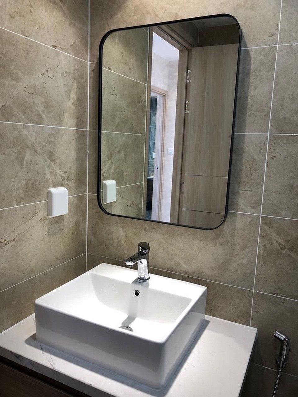 Large black-framed mirror above a white vessel sink in a tiled bathroom.