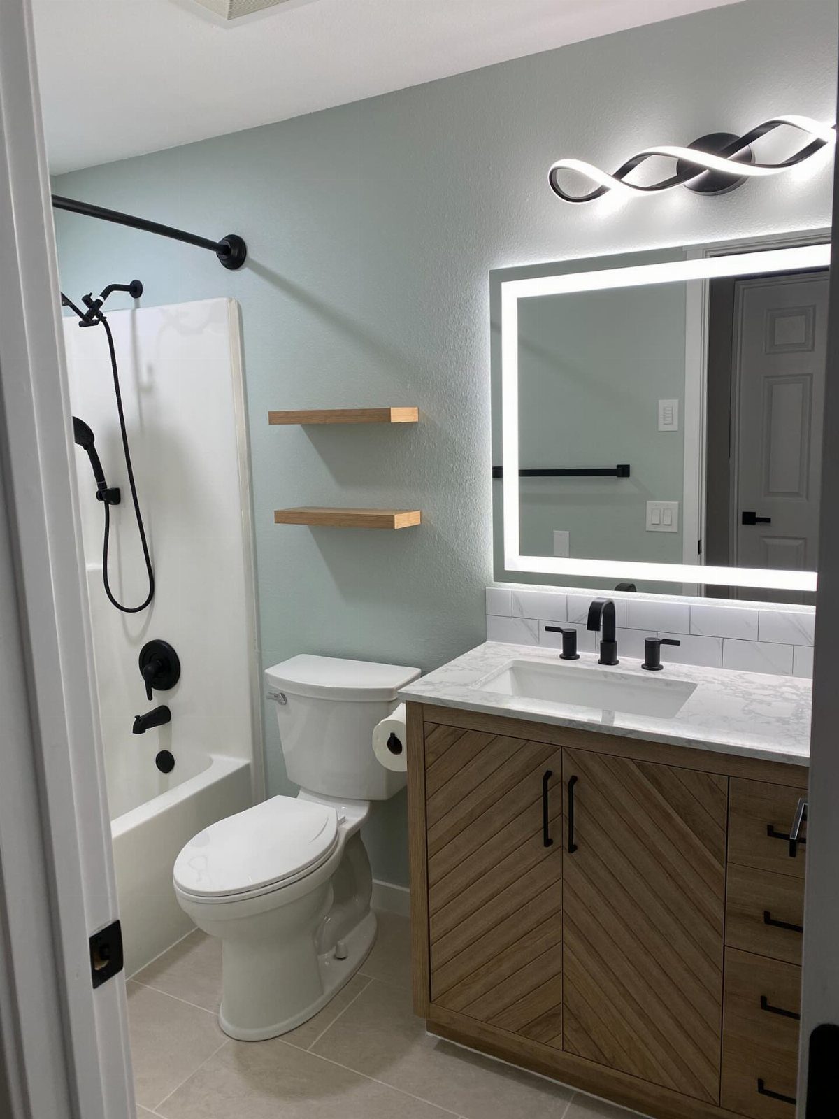 Small bathroom with light blue walls, wooden vanity, and white fixtures.