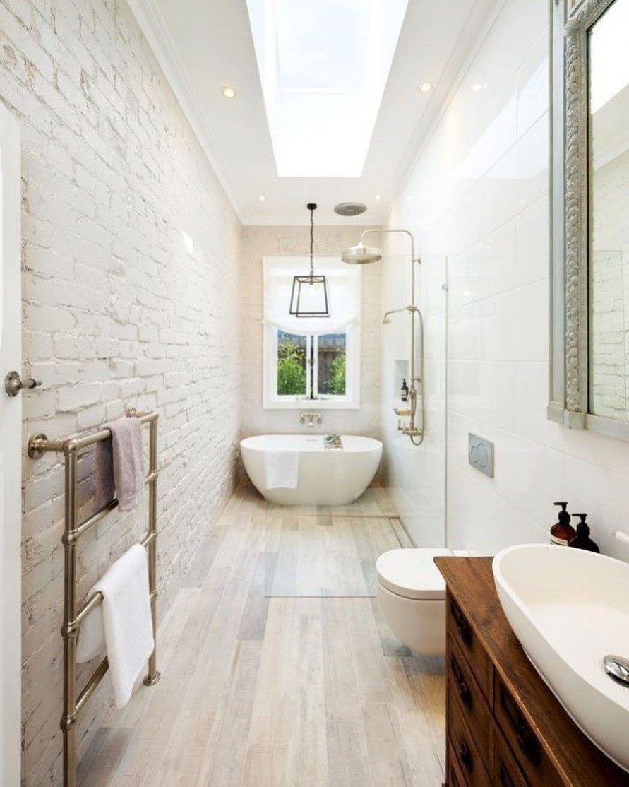 Bright narrow bathroom with a skylight, window, white brick wall, and freestanding tub.