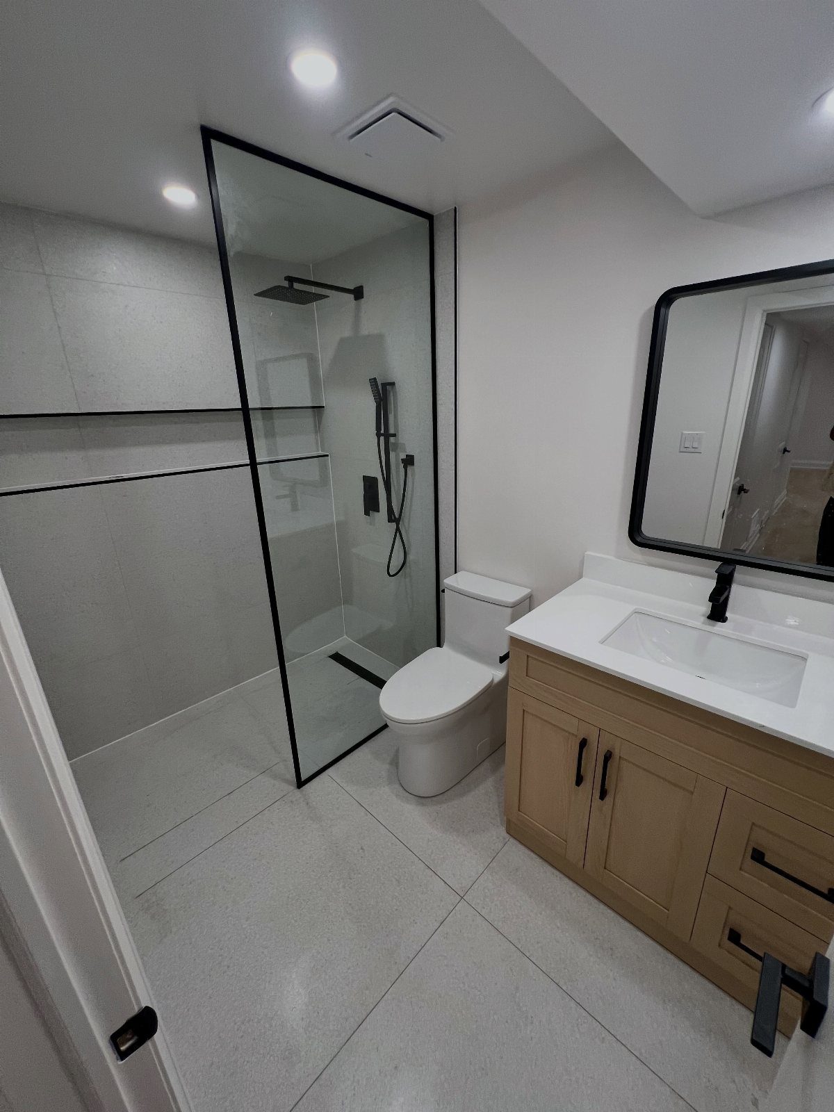 Modern small bathroom with a glass walk-in shower, white toilet, and wood vanity.