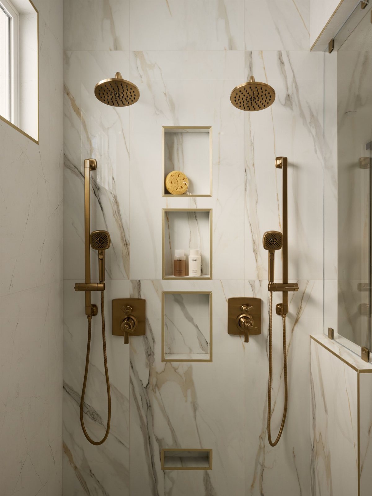 Dual gold shower heads and handheld sprayers on white marble walls with niches.