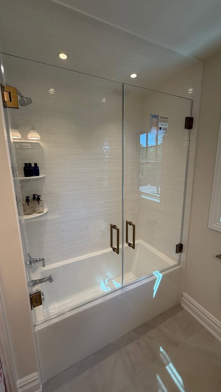 White bathtub with a frameless glass shower enclosure and gold hardware in a bathroom.