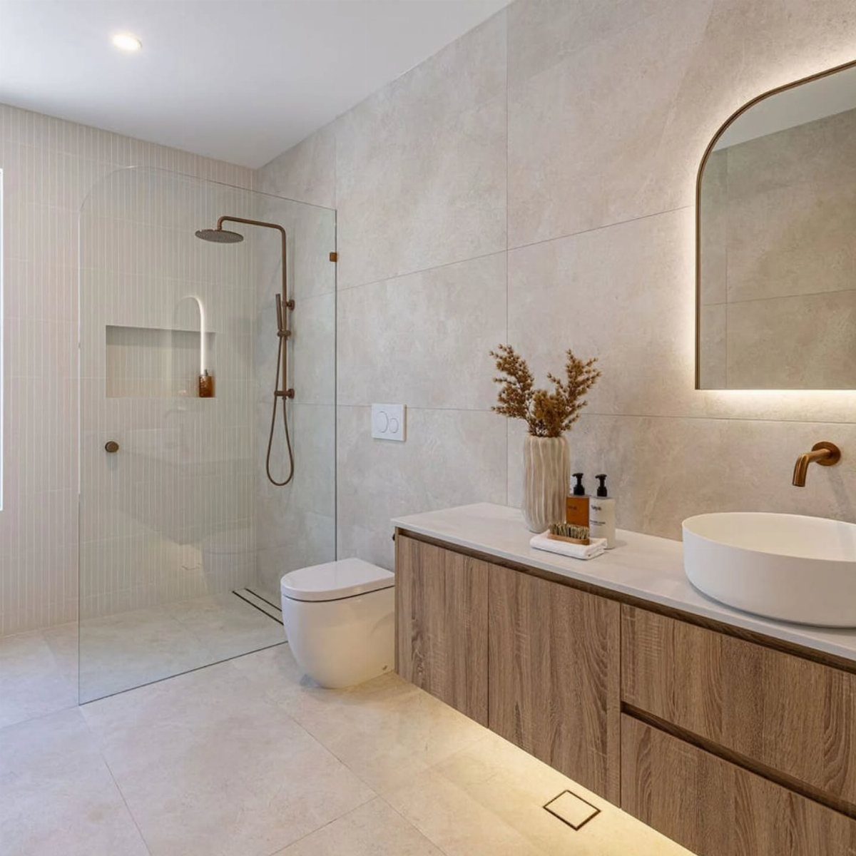 Modern bathroom with large beige tiles, glass shower, and wooden vanity sink.