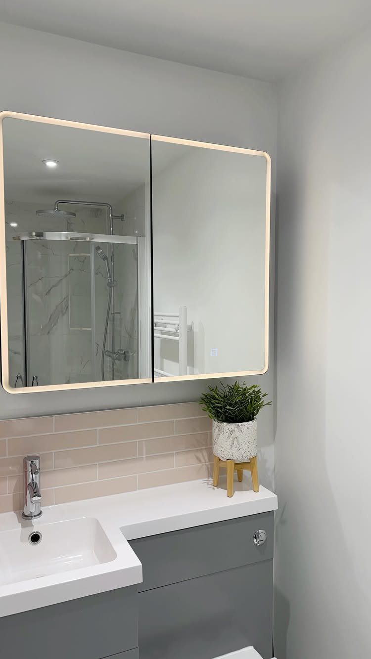 Mirrored cabinet with integrated lighting above a grey bathroom vanity and white sink.