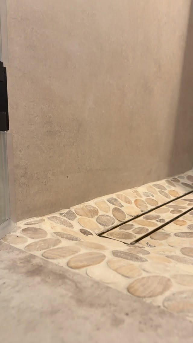 River stone shower floor with a linear drain and beige textured walls.