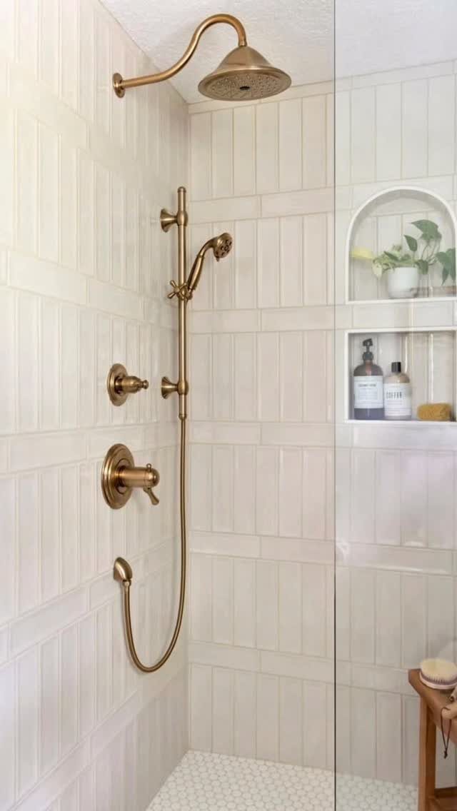 Gold shower fixtures against white vertical wall tiles with a recessed arched niche.