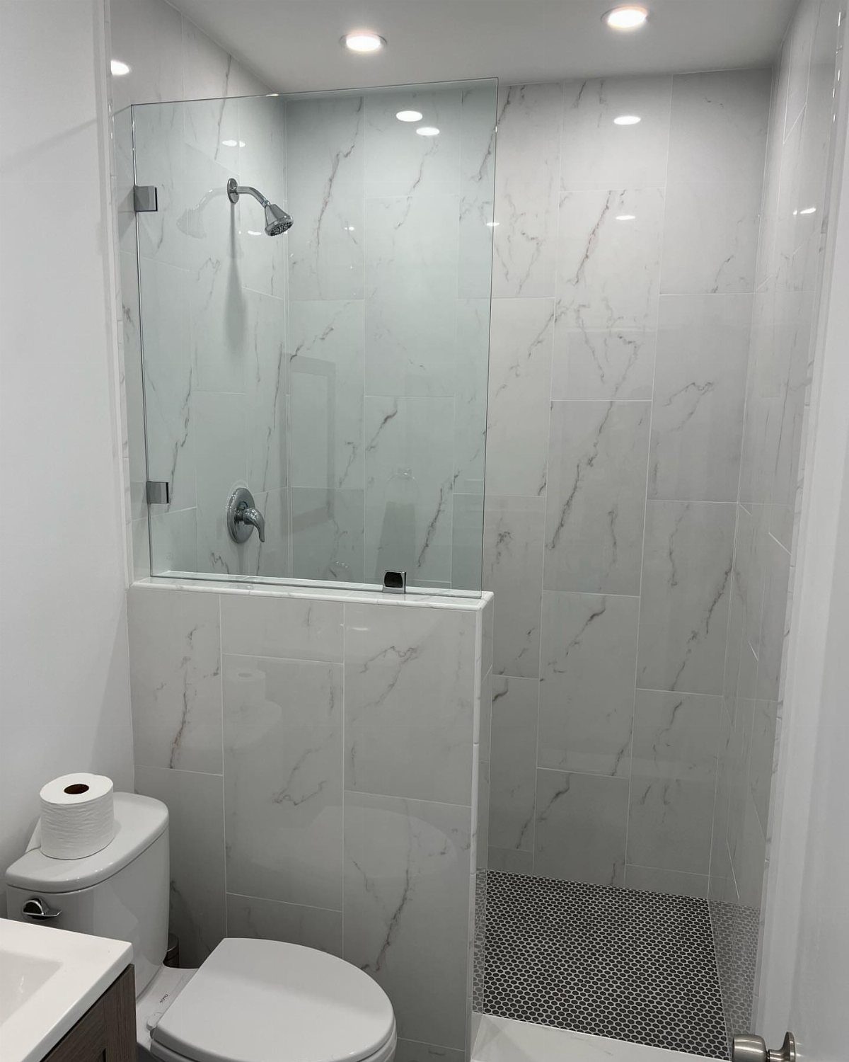 Walk-in shower with frameless glass and white marble tiles in a small bathroom