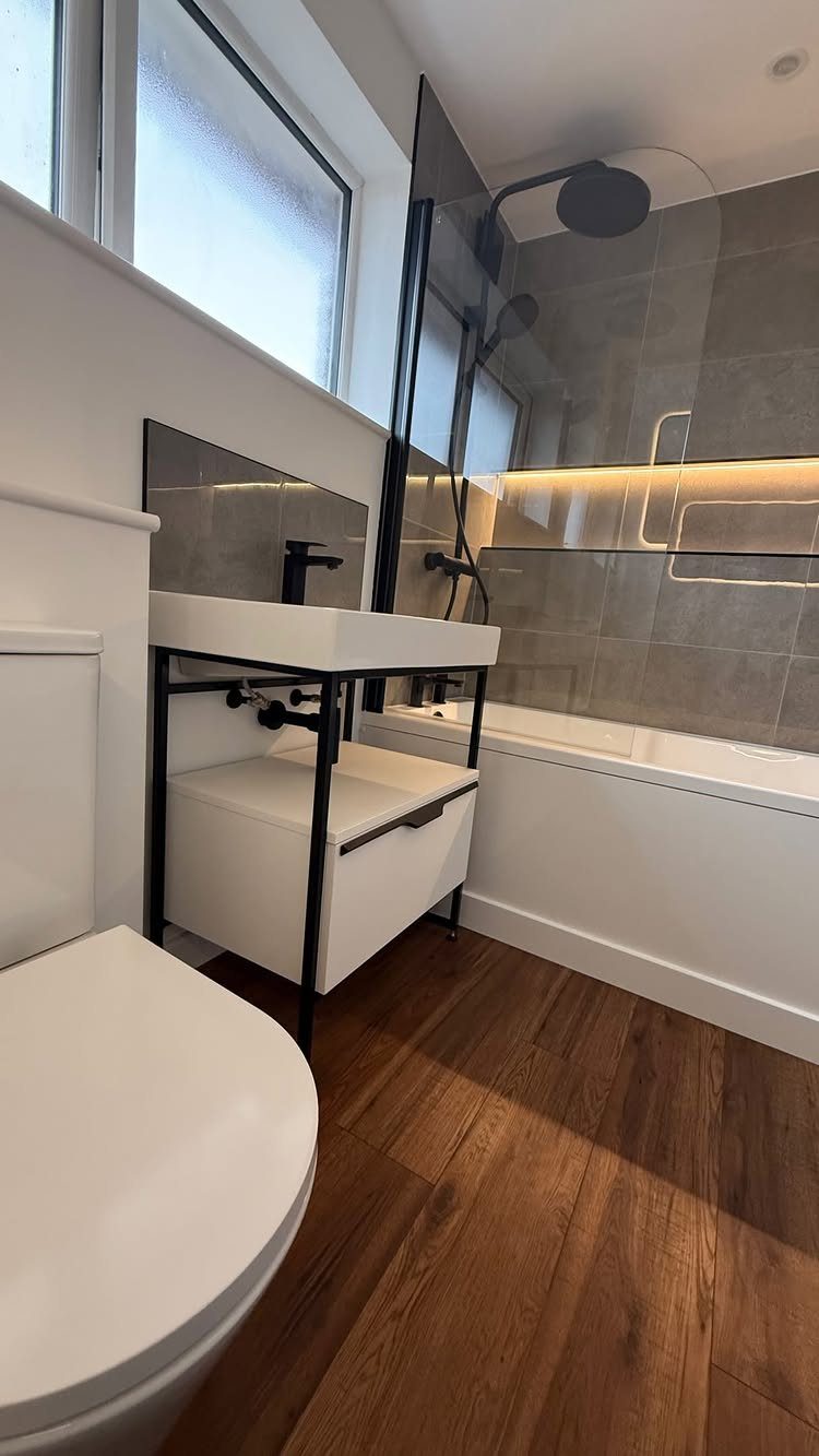 Brown wood-effect plank flooring in a modern bathroom with white fixtures and grey tiles.