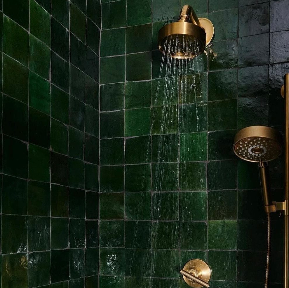 Dark green glossy wall tiles with gold shower fixtures and running water.