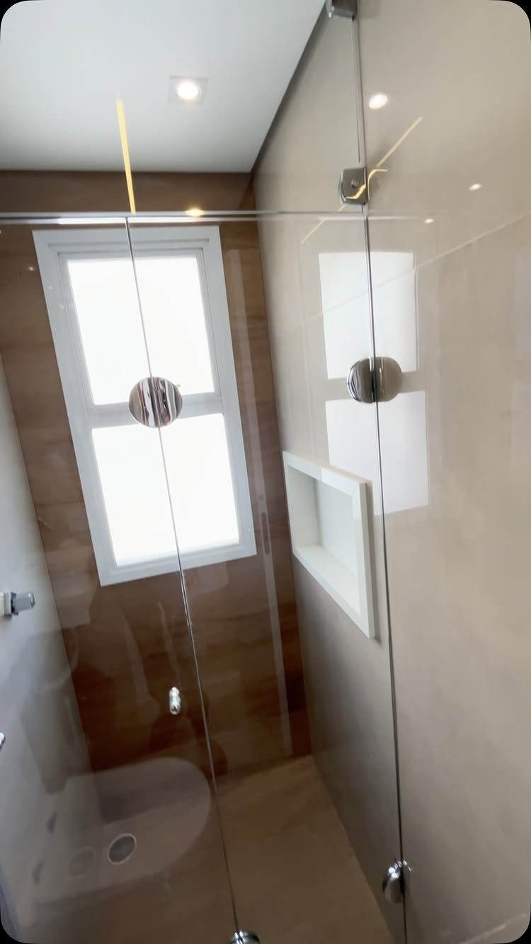 Glass shower door in a modern bathroom with beige walls and frosted window