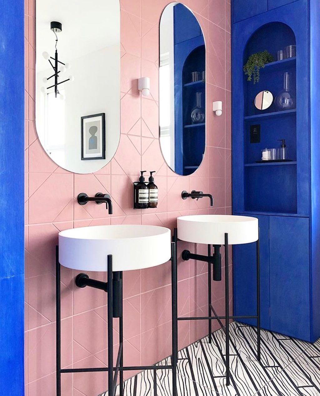 Pink diamond-patterned wall tiles in a bathroom with blue shelving and white sinks.