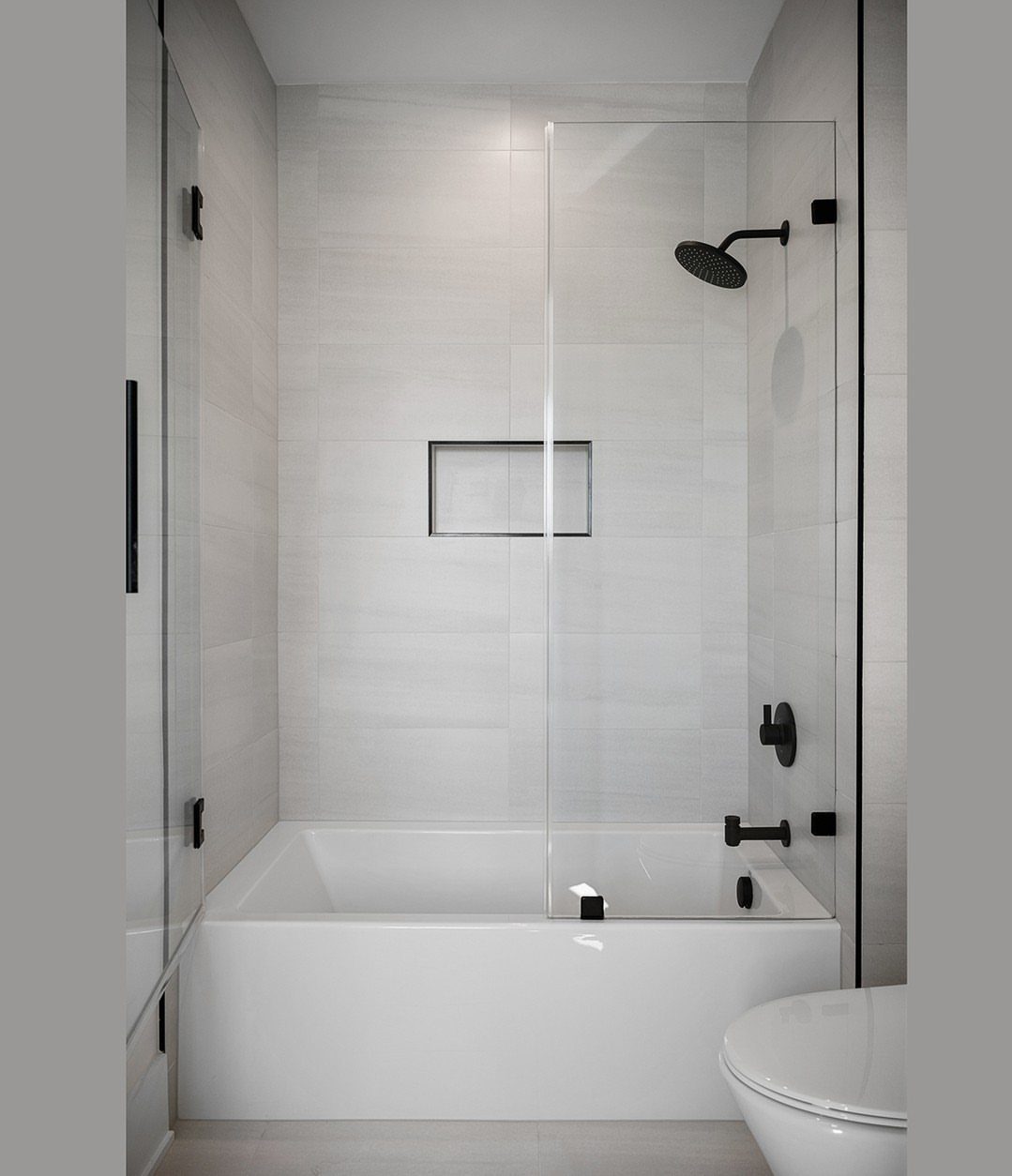 White alcove bathtub with a frameless glass panel and black shower fixtures.
