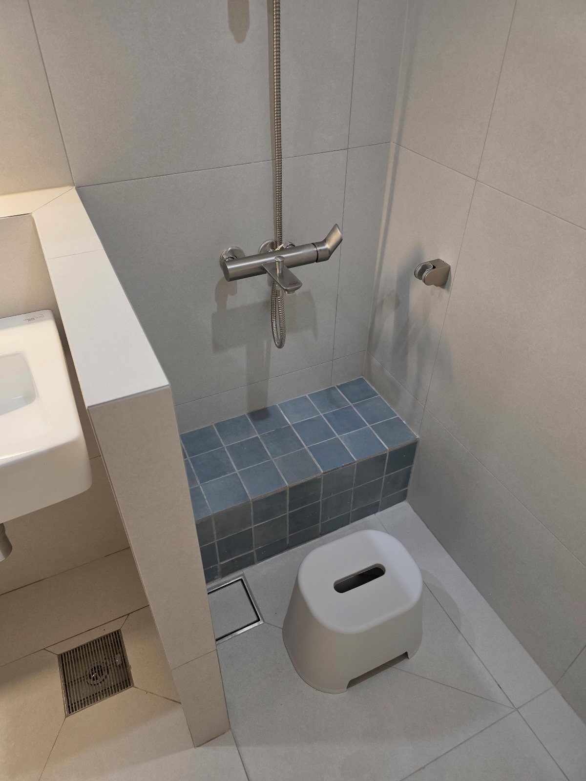 Built-in blue tiled bench in a small grey bathroom with shower fixtures.