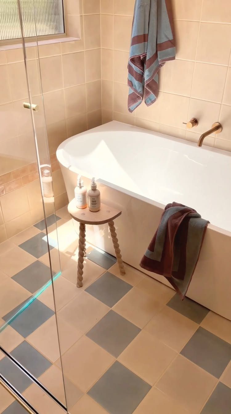 White freestanding bathtub in a small bathroom with checkered blue and beige floor tiles.