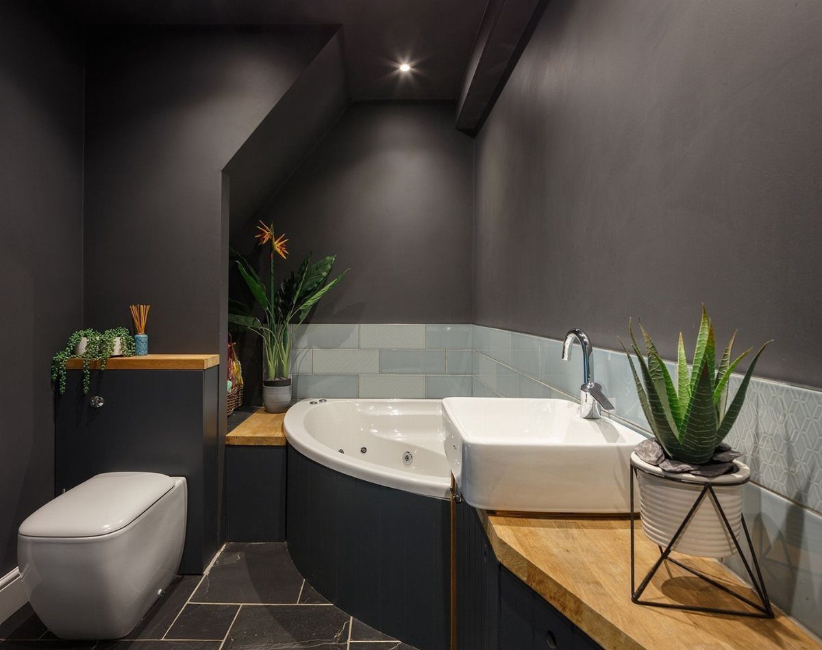White corner bathtub and vessel sink in a dark grey modern small bathroom.