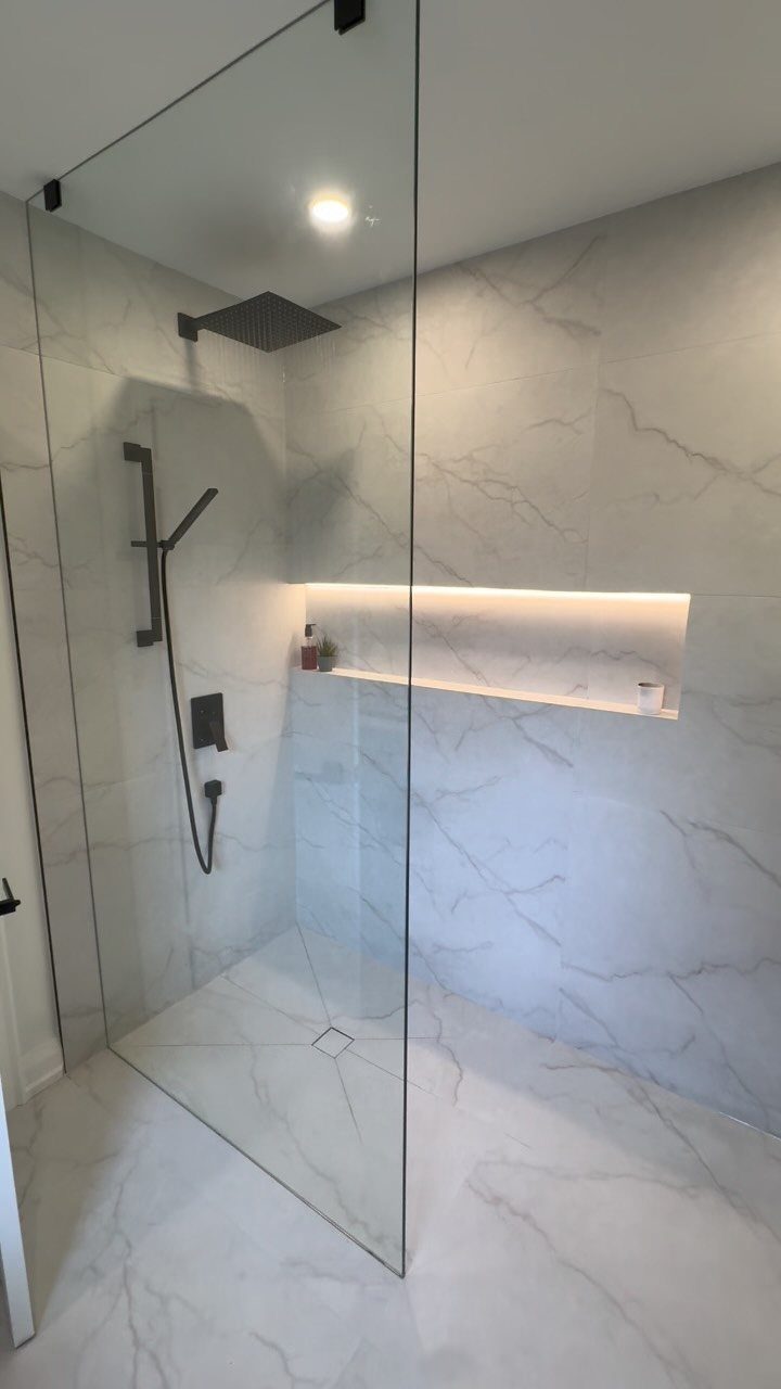 Walk-in curbless shower with white marble tiles and a frameless glass panel.