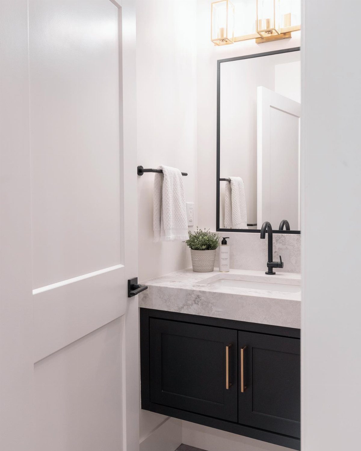 Black floating vanity with marble top and gold handles in a white bathroom