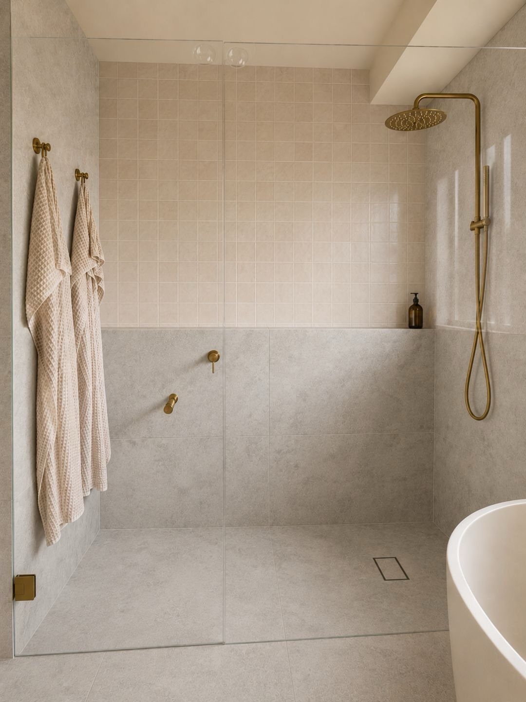 Walk-in shower with frameless glass panel, gold fixtures, and white freestanding bathtub.