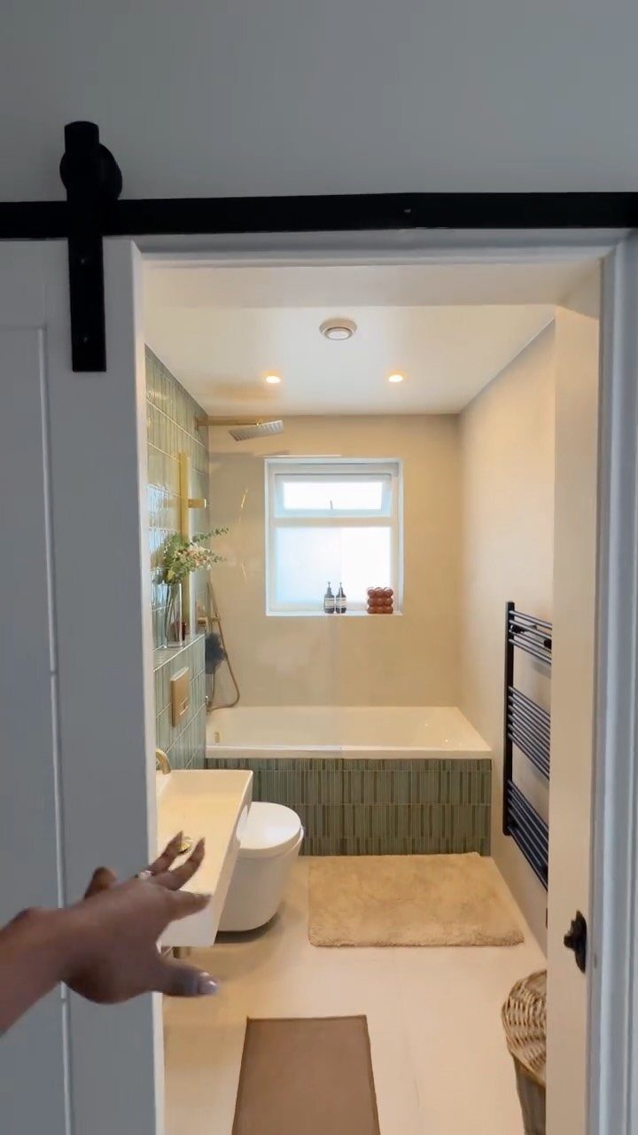 Small bathroom with a white bathtub, green tiling, and a black towel radiator.