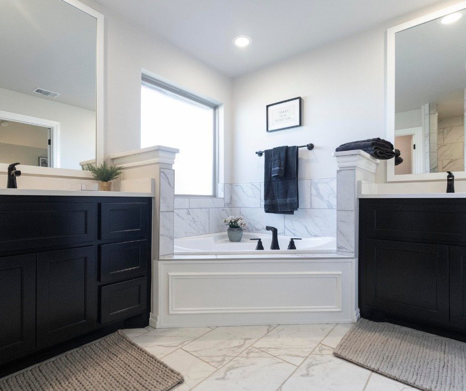 White built-in bathtub between two black vanities in a bright marble bathroom.