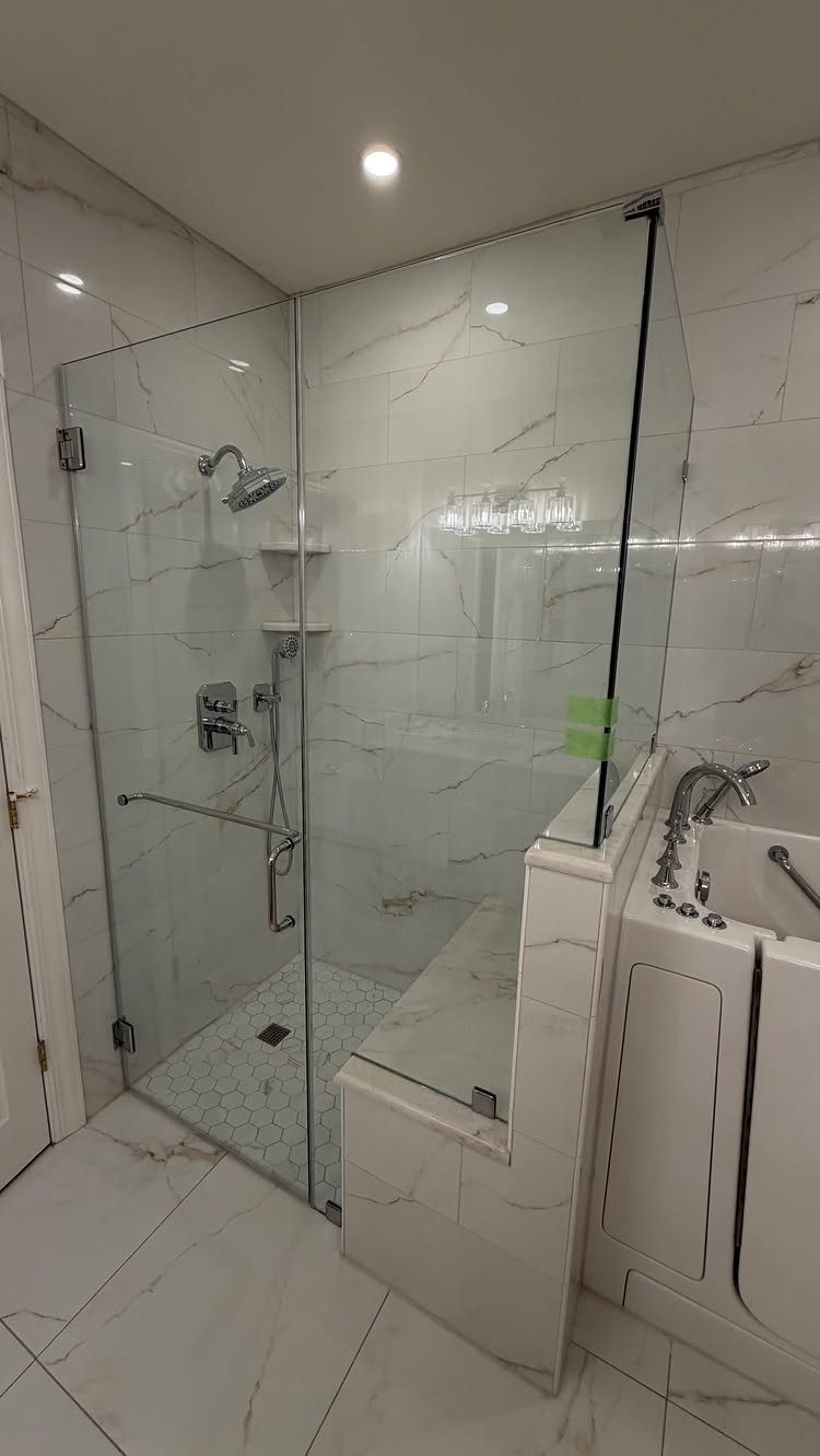 White marble bathroom with a glass shower enclosure and a built-in bathtub.